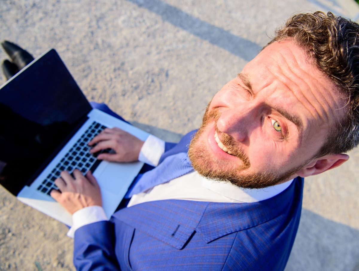 Man smiling cheerful face work with laptop close up. Businessman formal suit looks back while holds open screen laptop. Pleasant workday outdoors. Sunny summer day great opportunity to work outside.